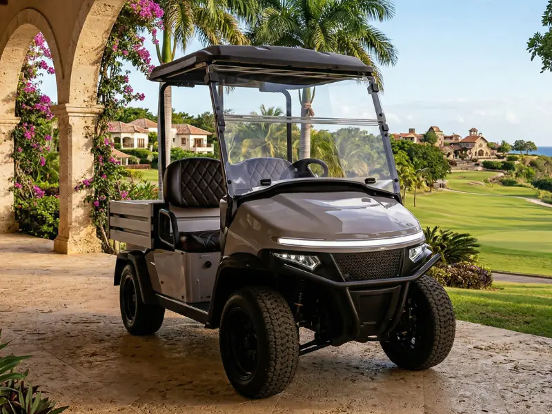 Carrito de golf utilitario eléctrico Denago Oxen gris con caja de carga abierta y llantas todoterreno bajo una arcada de piedra