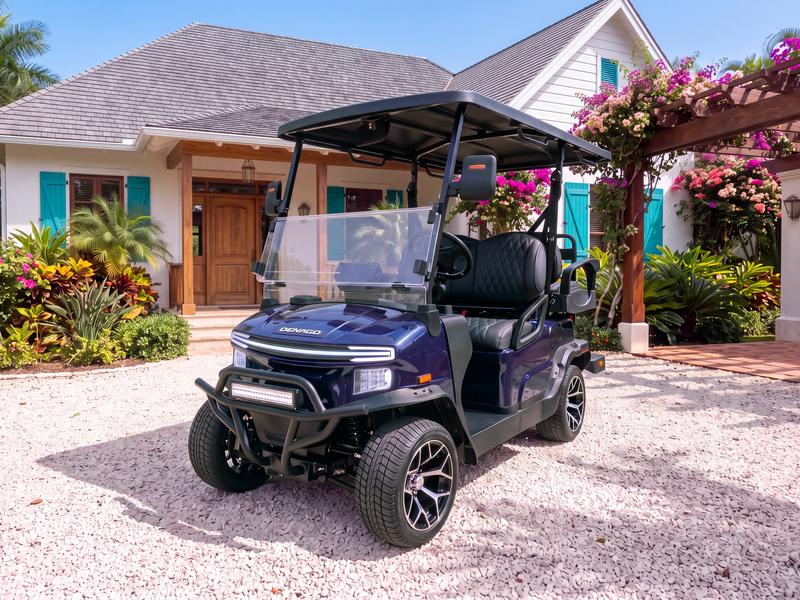 Denago Nomad four-seat electric golf cart in navy blue on a white coral gravel driveway in front of a cottage-style villa with turquoise shutters and a bougainvillea pergola in Casa de Campo
