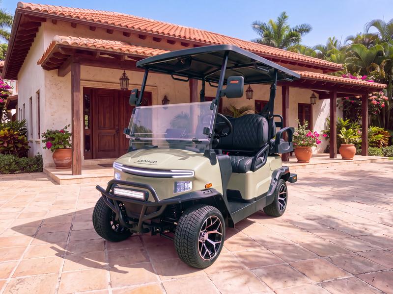 Denago Nomad four-seat electric golf cart in khaki on a sandstone driveway in front of a single-story hacienda-style villa with a covered porch, wooden beams and terracotta pots in Casa de Campo