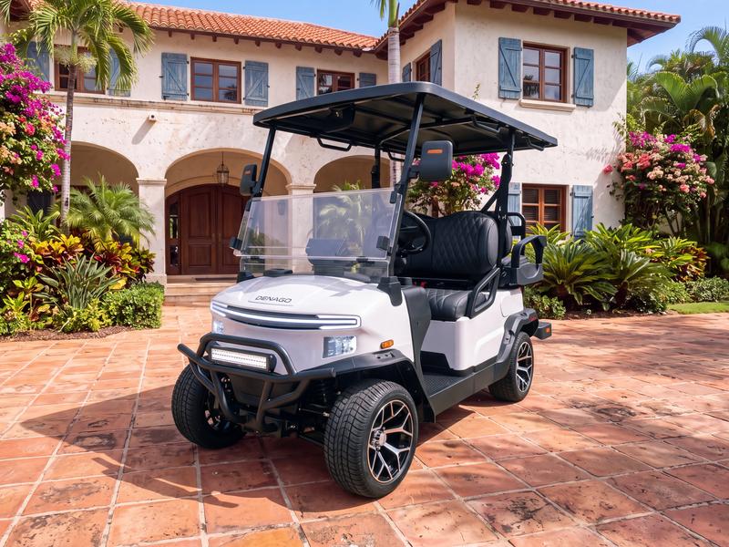 Denago Nomad four-seat electric golf cart in white on a terracotta tile driveway in front of a two-story Mediterranean villa with an arched loggia and blue wooden shutters in Casa de Campo