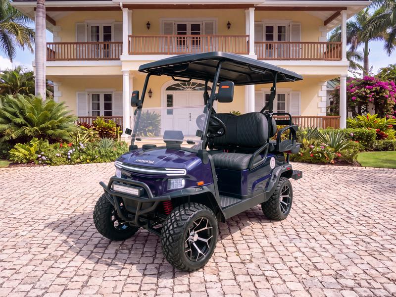 Denago Nomad XL lifted four-seat electric golf cart in navy blue on a cobblestone driveway in front of a pale yellow two-story colonial villa with white trim and wooden balconies in Casa de Campo