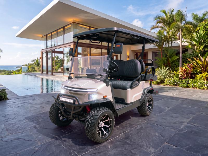Denago Nomad XL lifted four-seat electric golf cart in champagne on a dark slate terrace beside a glass-walled modern villa with an infinity pool overlooking the sea in Casa de Campo