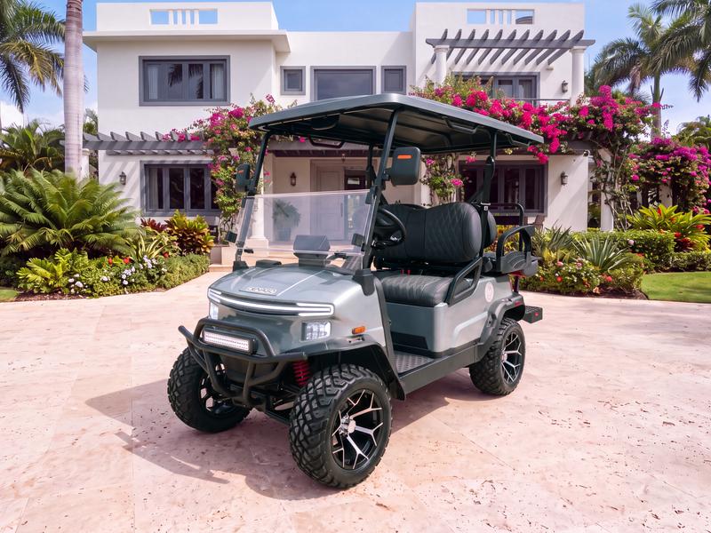 Denago Nomad XL lifted four-seat electric golf cart in grey on a light stone driveway in front of a white villa with dark grey window frames and a bougainvillea pergola in Casa de Campo