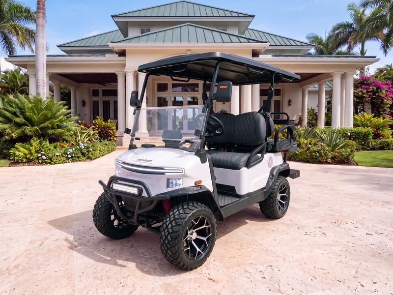 Denago Nomad XL lifted four-seat electric golf cart in white on a travertine driveway in front of a Caribbean villa with white columns and a green metal roof in Casa de Campo