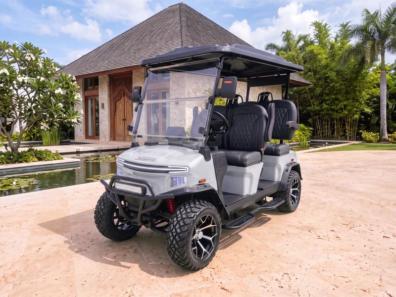 Denago Rover XL four-seat electric golf cart in grey in front of a Balinese-style villa with a steep dark roof, carved wooden doors and a lily pond in Casa de Campo