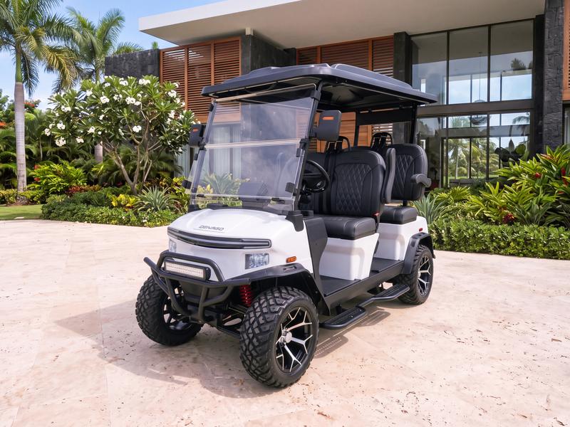 Denago Rover XL four-seat electric golf cart in white on a travertine driveway in front of a modern villa with dark stone walls and teak louvers in Casa de Campo