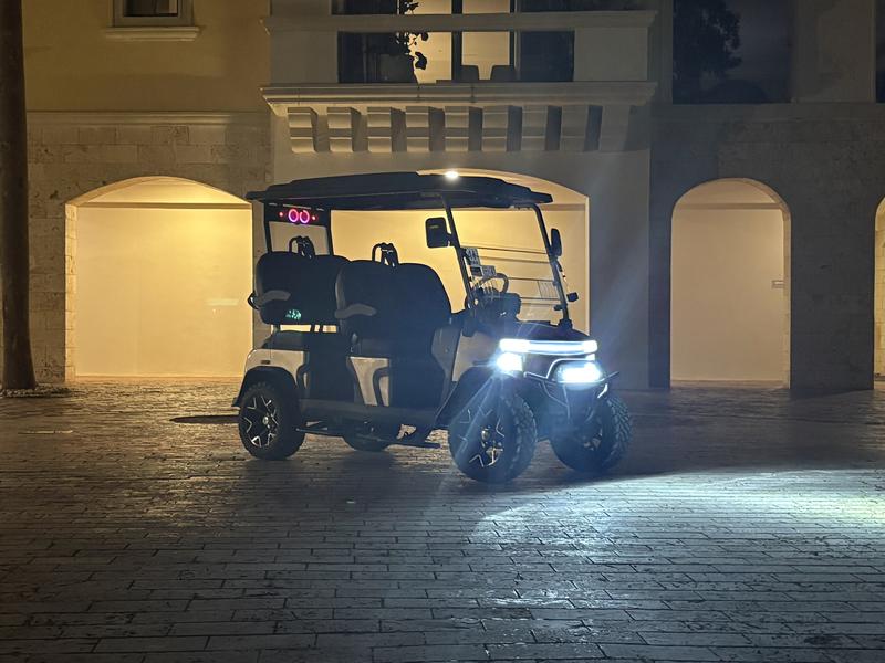Denago golf cart at night with its LED light strip, headlights and LED light bar on, parked in front of a lit stone arcade
