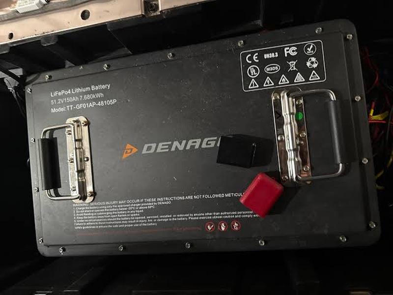 Denago LiFePO4 lithium battery in a golf cart, labelled 51.2V 150Ah 7.680kWh, with carry handles and the Denago logo