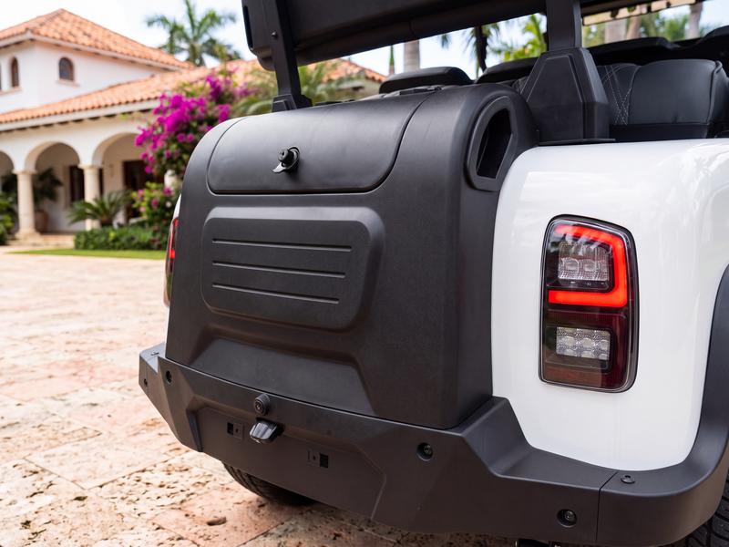 Rear storage box with a latched lid on the back of a white Denago golf cart, parked in front of a villa in Casa de Campo