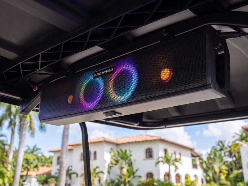 Bluetooth soundbar with glowing LED speaker rings under the roof of a Denago golf cart, with a villa in Casa de Campo behind it